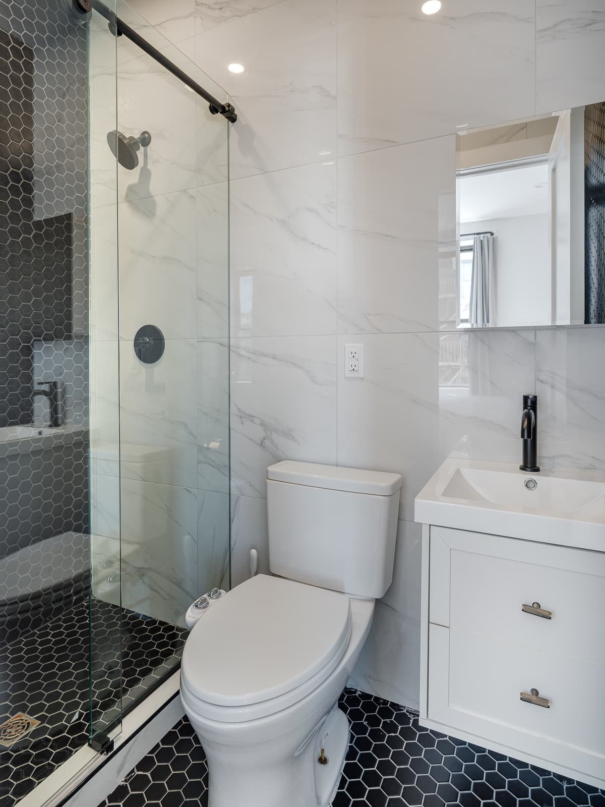 Marble-tiled bathroom with glass walk-in shower and black hexagon floor