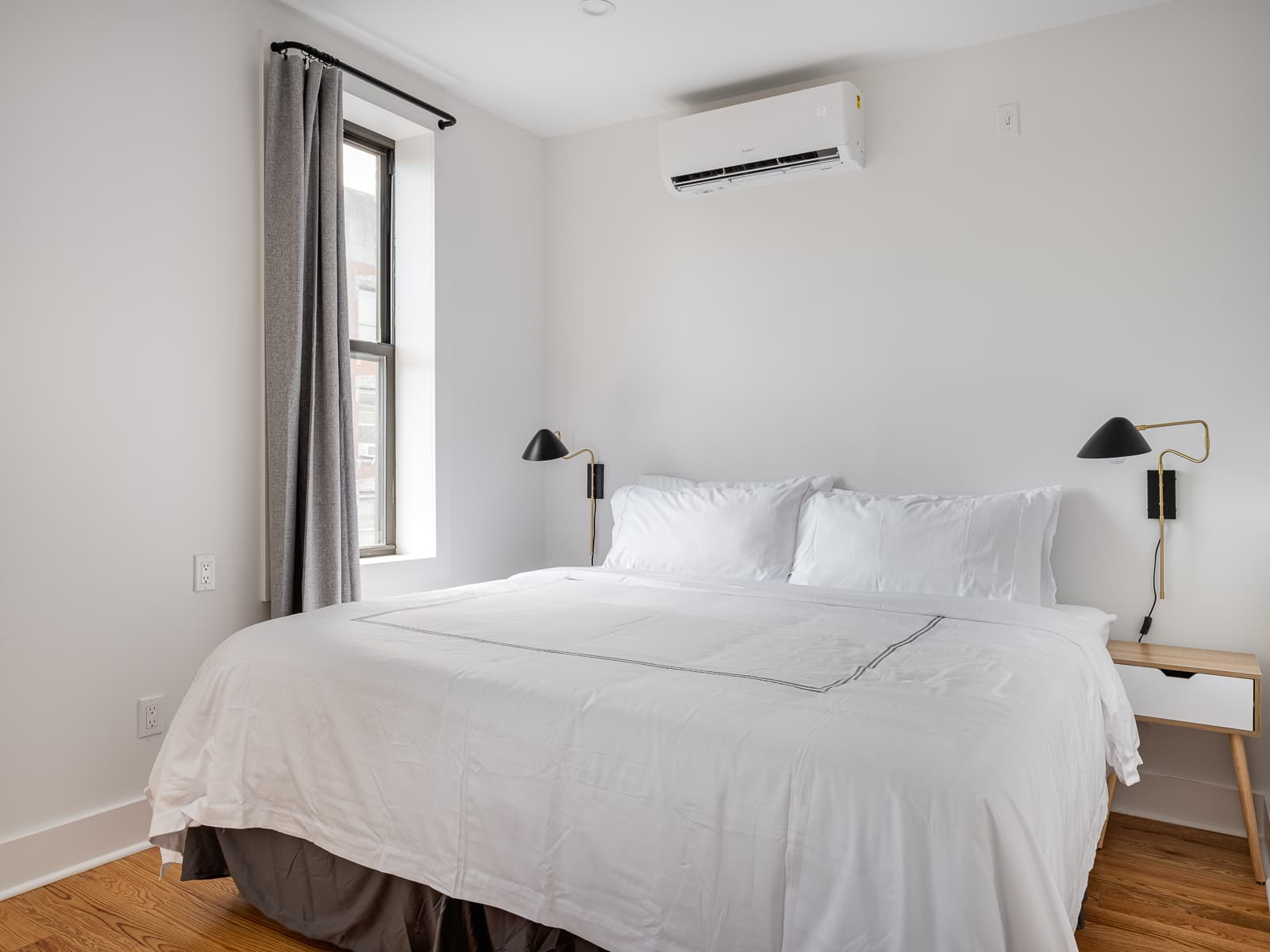 Large bed with white hotel linens between black-and-brass swing-arm sconces